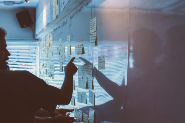 person pointing to post-it notes on a whiteboard