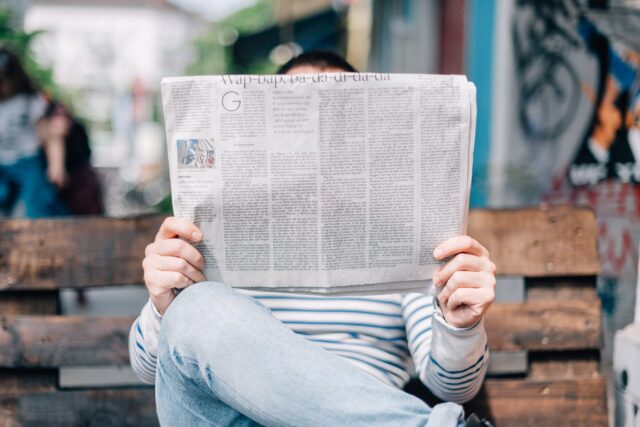 person sitting on a bench reading a newspaper