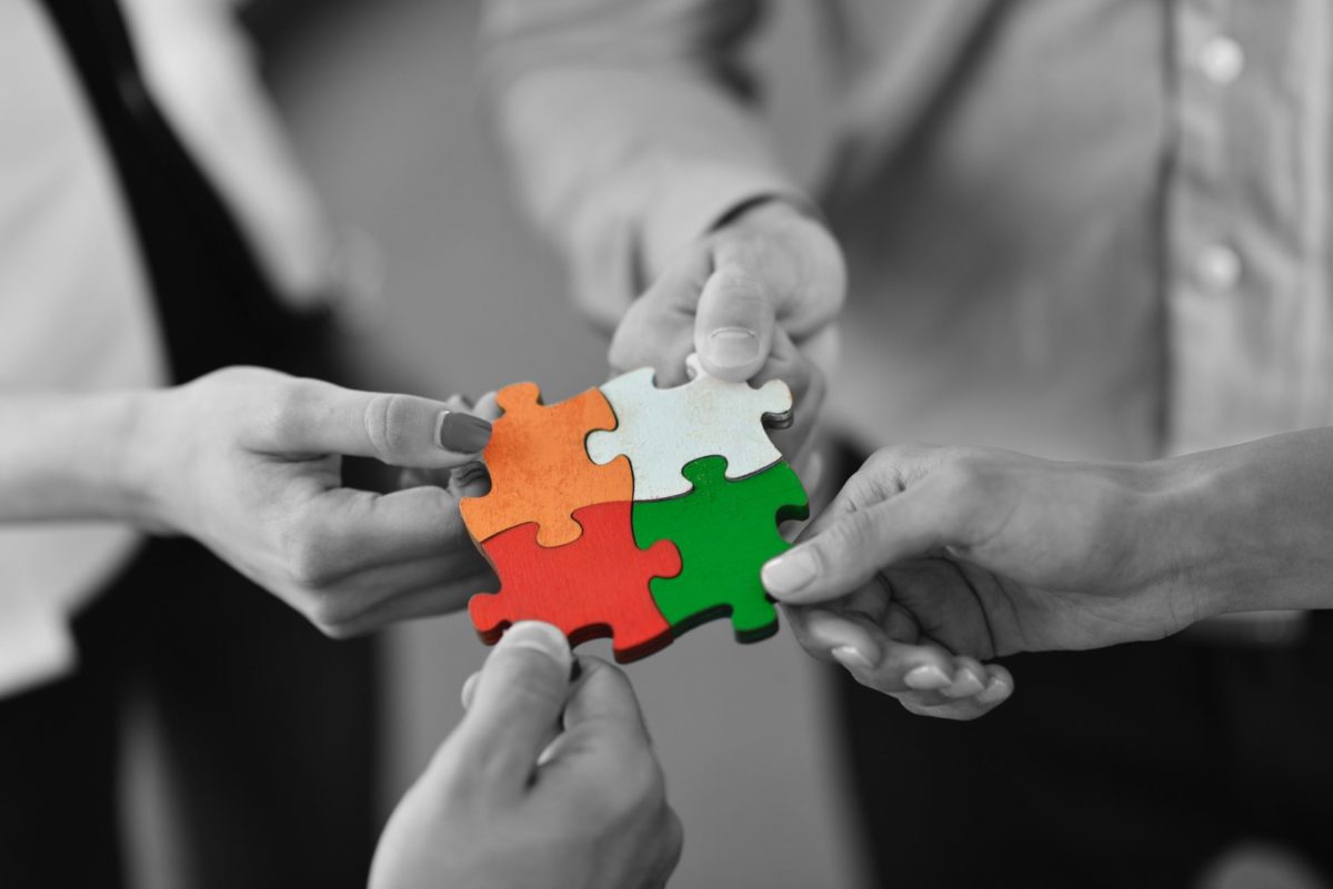 4 people in black and white putting coloured puzzle pieces together