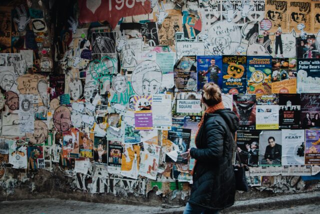 posters and graffiti on a wall with woman looking