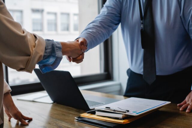 Two people shaking hands over a desk