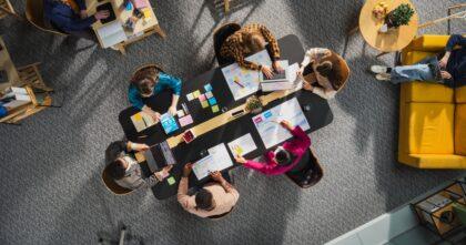 A top-down view of a modern office and team sitting around a table.