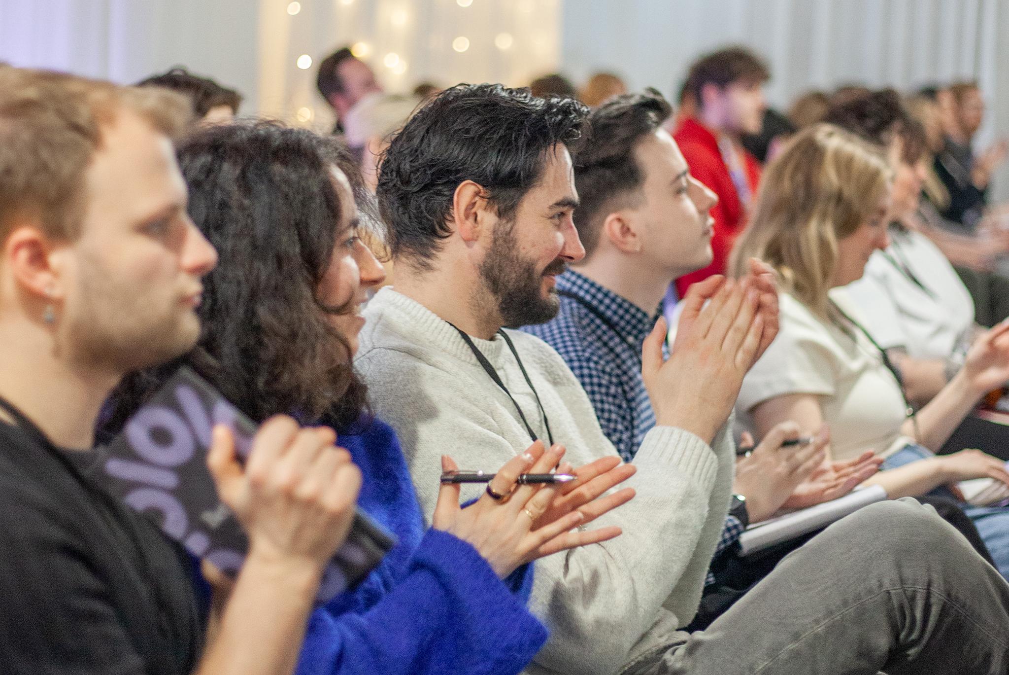 Audience members seated in rows applauding and smiling at a conference or event